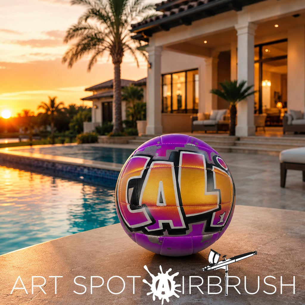 A colorful custom volleyball personalized with the word "CALI" painted on it, placed on a tiled surface near a pool and a palm tree, with a house and sunset in the background.