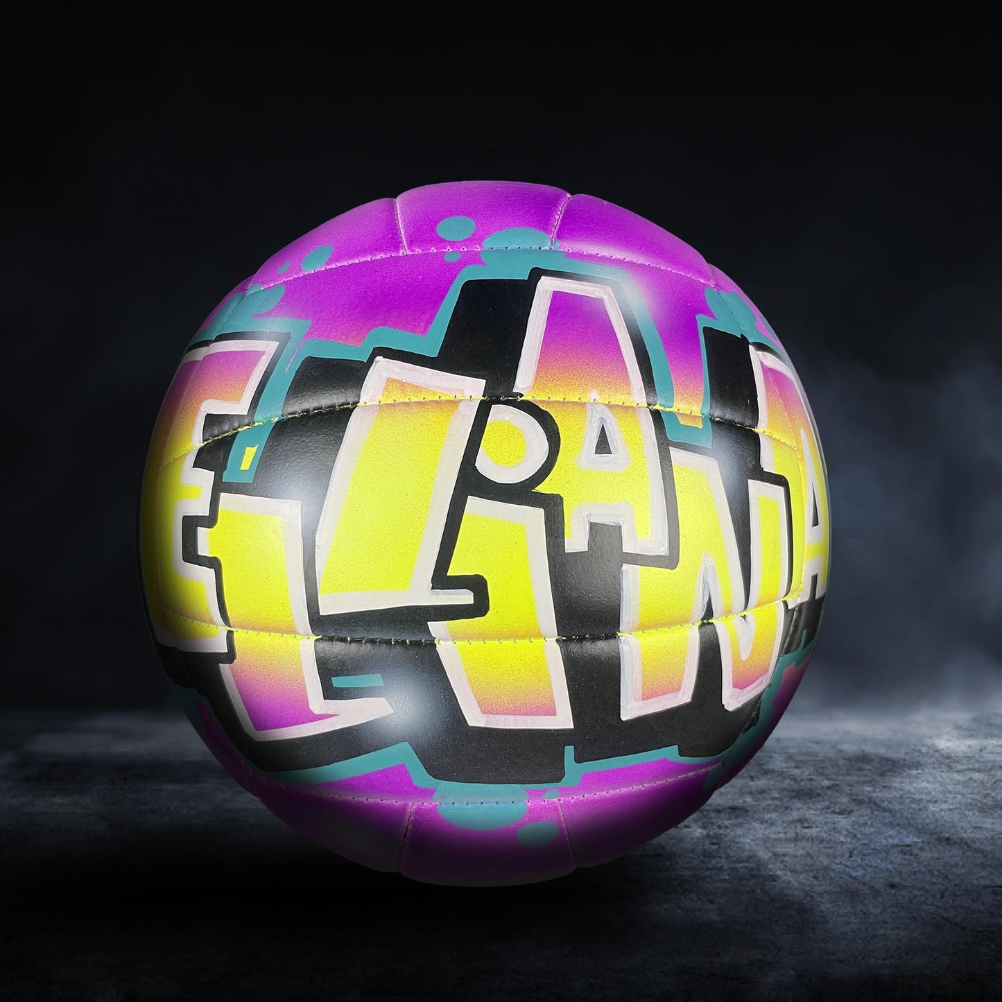 A colorful volleyball with graffiti-style text on it, set against a dark background.