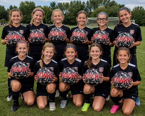 A group of young female soccer players posing together, holding soccer balls and smiling.