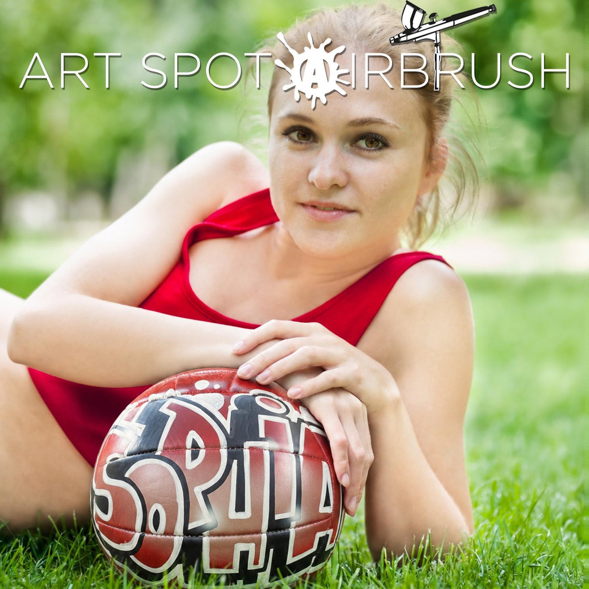 A woman in a red top is posing with a red and black custom volleyball personalized with a name in graffiti, sitting on a grassy field.