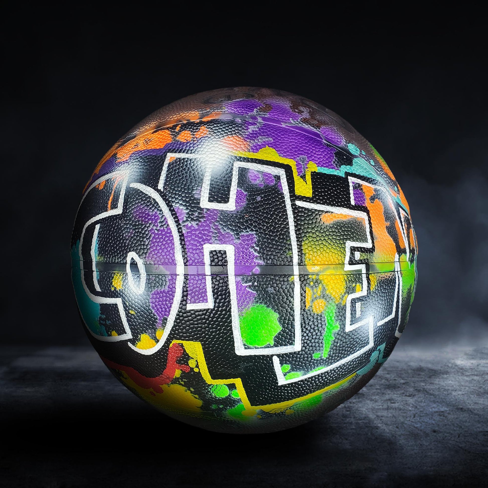 A colorful basketball with graffiti-style lettering on it, set against a dark background.