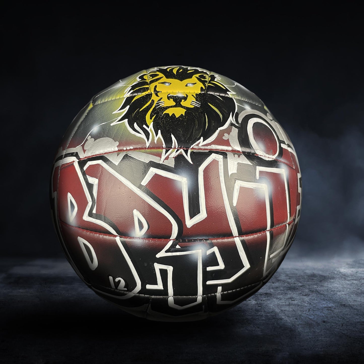 A soccer ball with a lion's head design on it, featuring a mix of red, black, and yellow colors.
