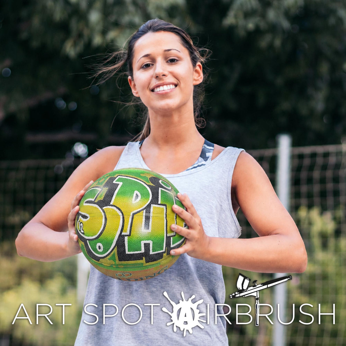 A woman is holding a green and yellow sports ball with the text "SPH" on it, smiling and posing for the camera.