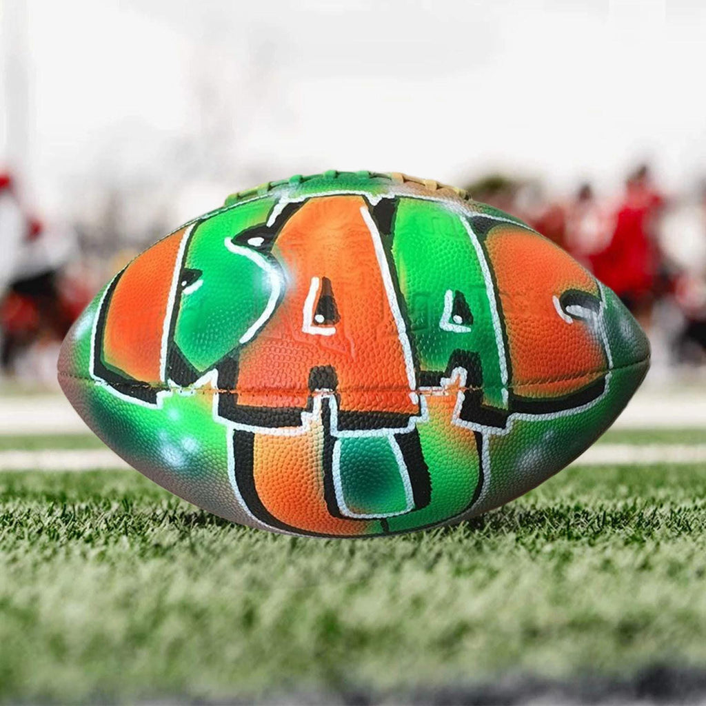 A football with the word "ISAAC U" painted on it, sitting on a grassy field.