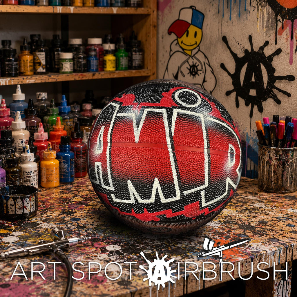 A basketball with the word "AMR" painted on it, sitting on a table surrounded by various art supplies and a graffiti-style wall in the background.