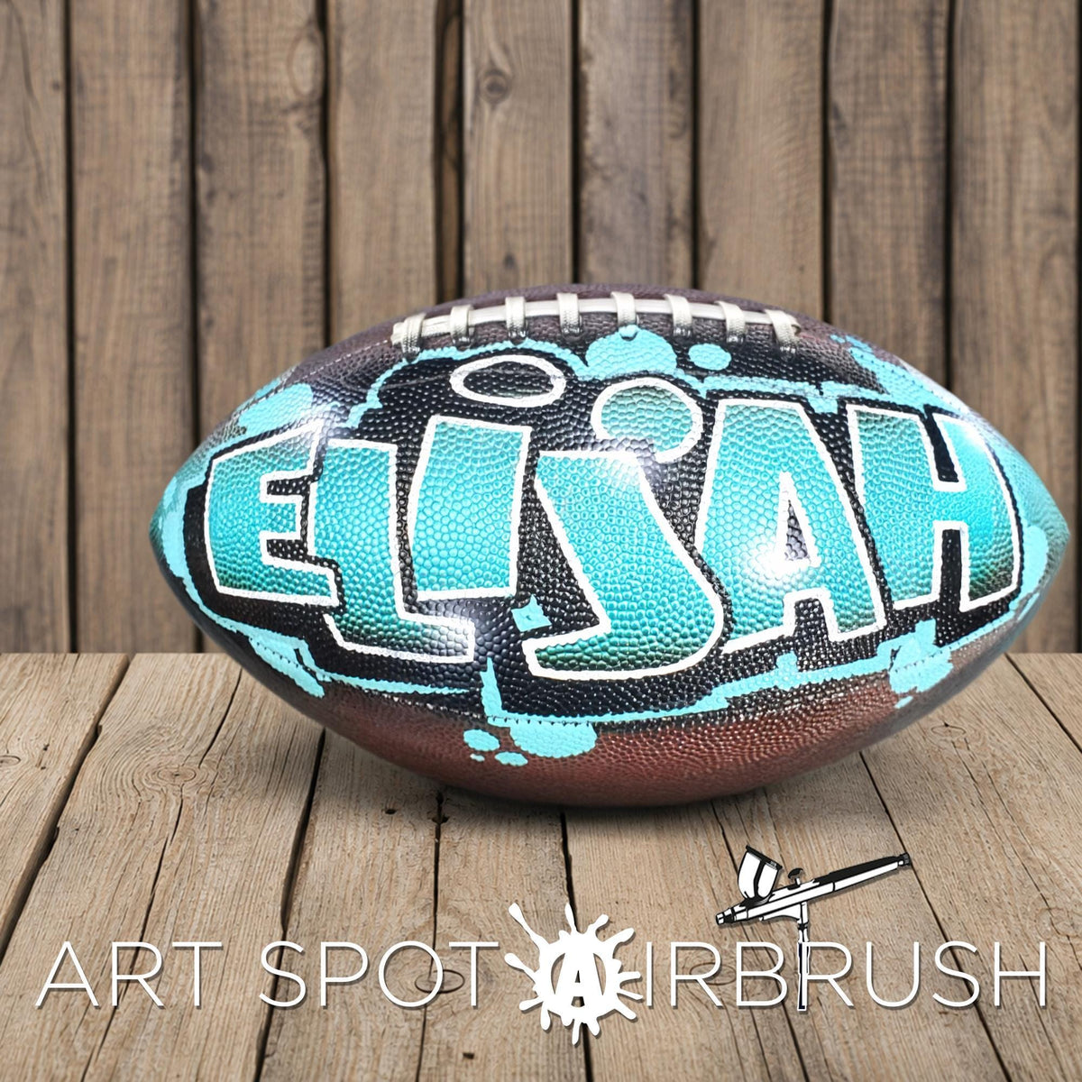 A football with the name "Elijah" painted on it, sitting on a wooden surface.