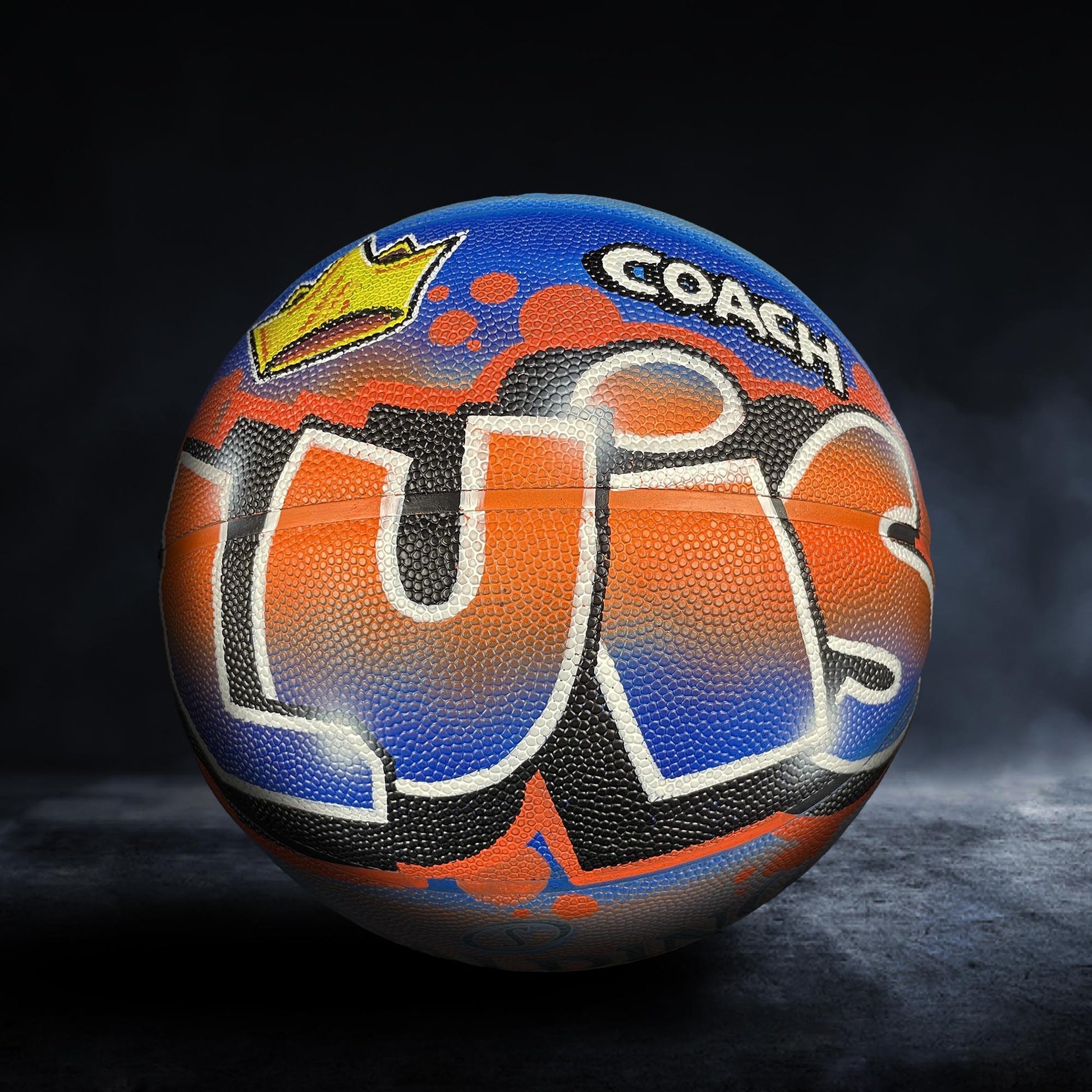 A basketball with the word "LUS" painted on it, featuring a crown and graffiti-style artwork.