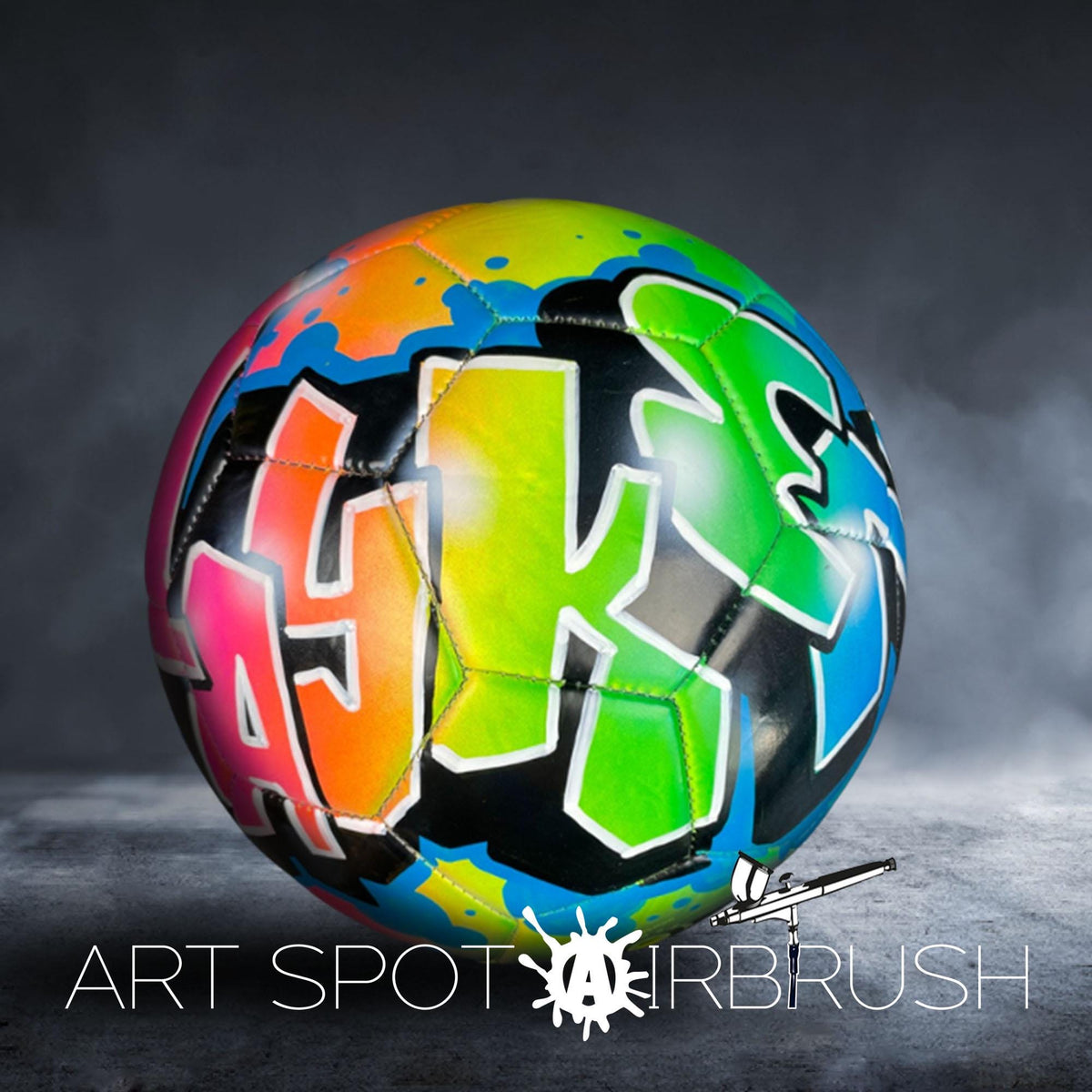 A colorful soccer ball with graffiti-style lettering on it, placed on a dark surface.