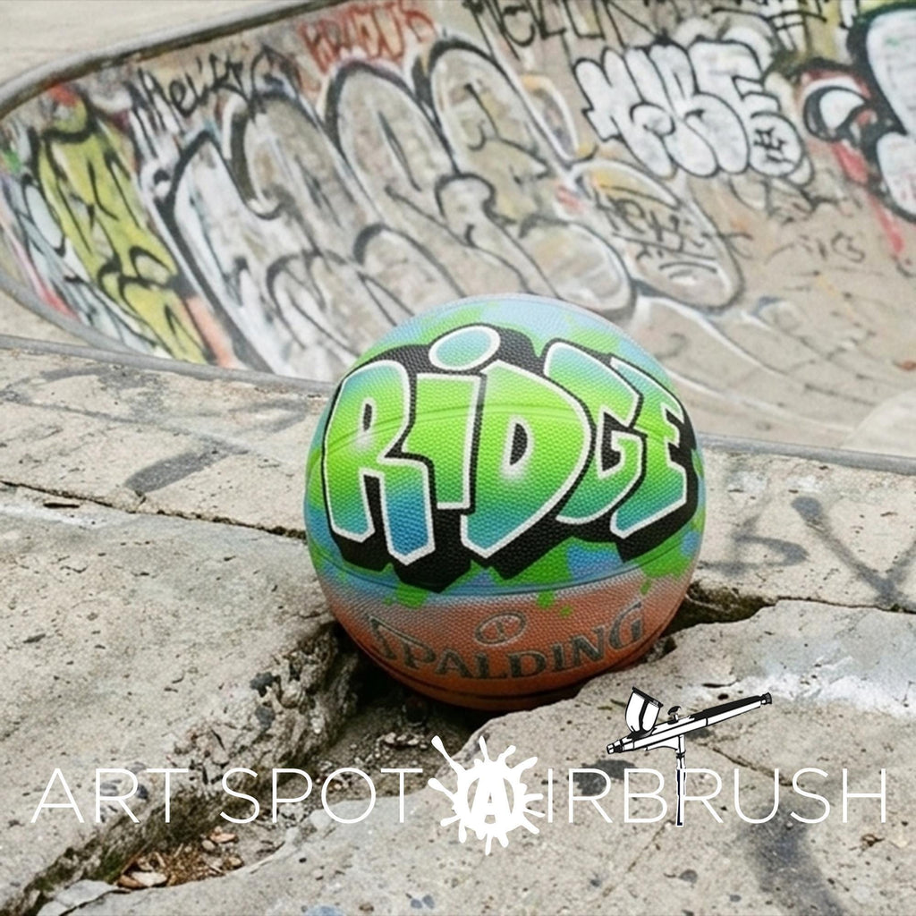 A colorful basketball with the word "RIDGE" painted on it, sitting on a concrete surface with graffiti in the background.