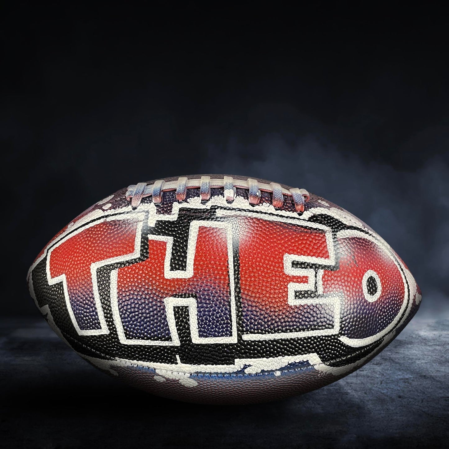 A football with the word "THE" written on it, against a dark background with smoke.