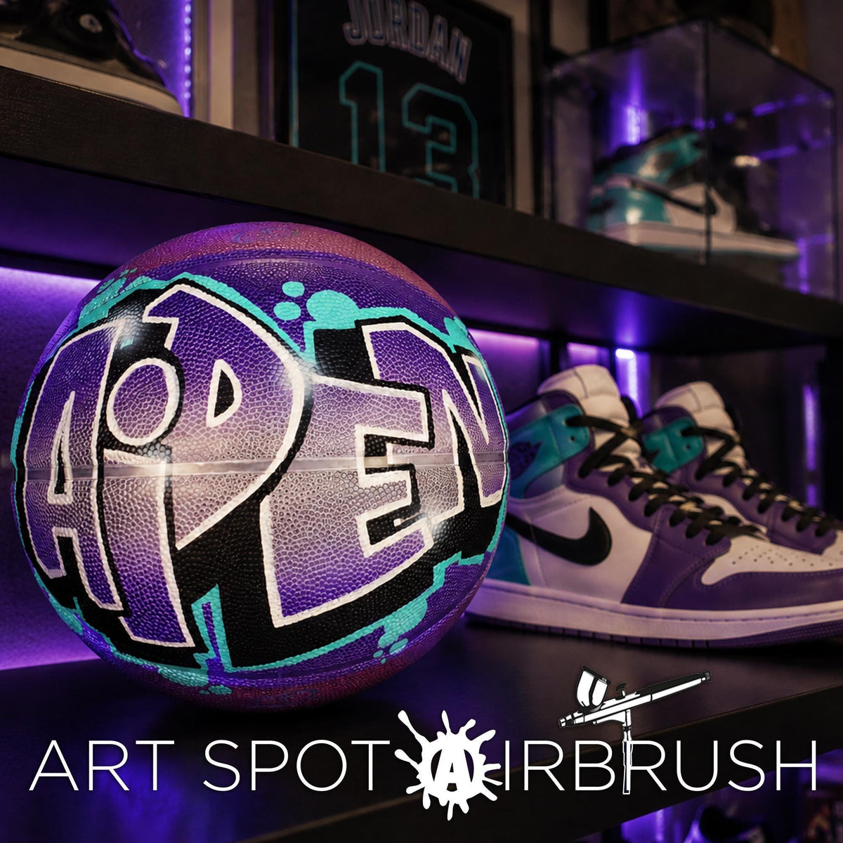A purple basketball with the word "PEN" painted on it, along with a pair of purple and white sneakers, displayed on a shelf.