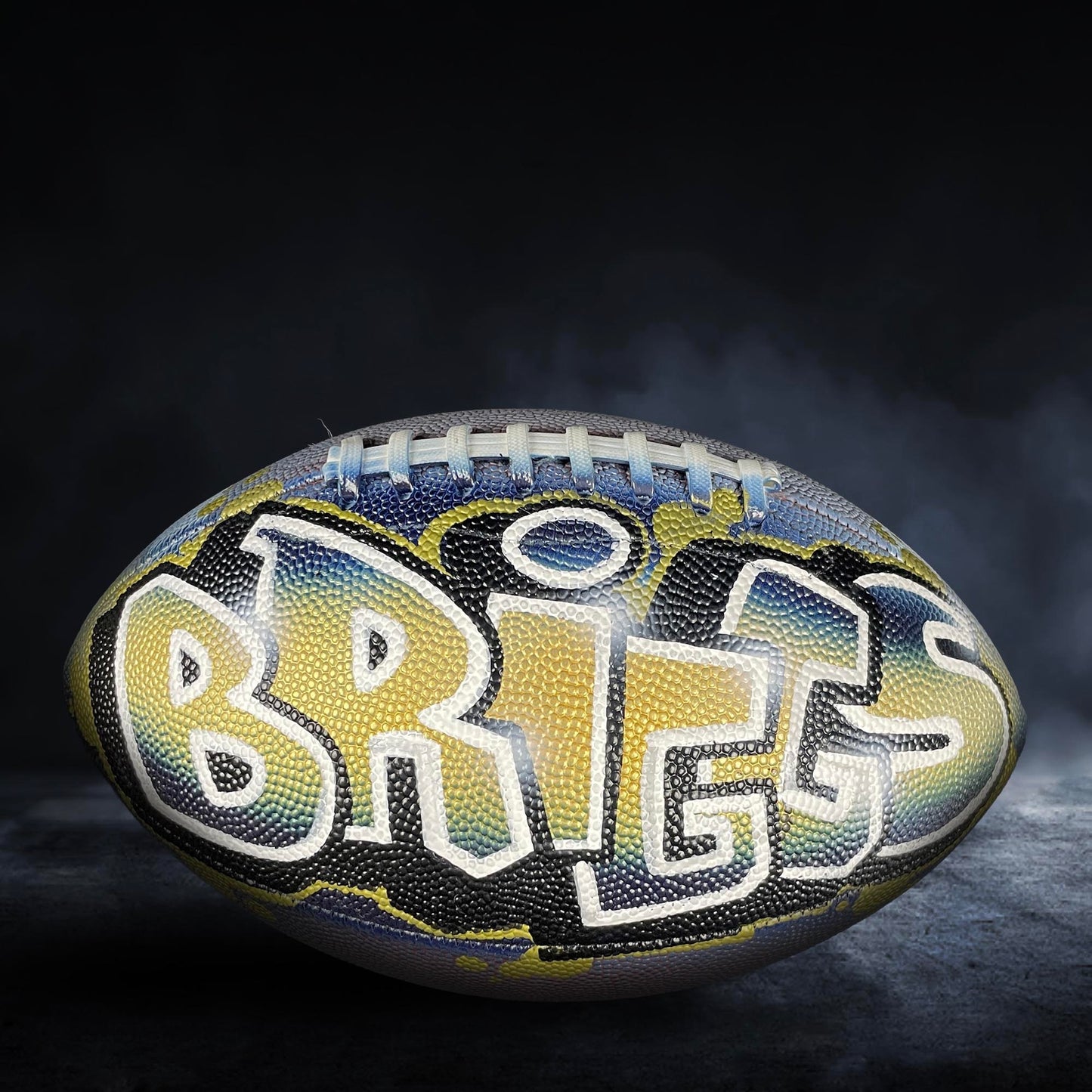 A football with the word "BRITT" painted on it, set against a dark background with smoke or fog.