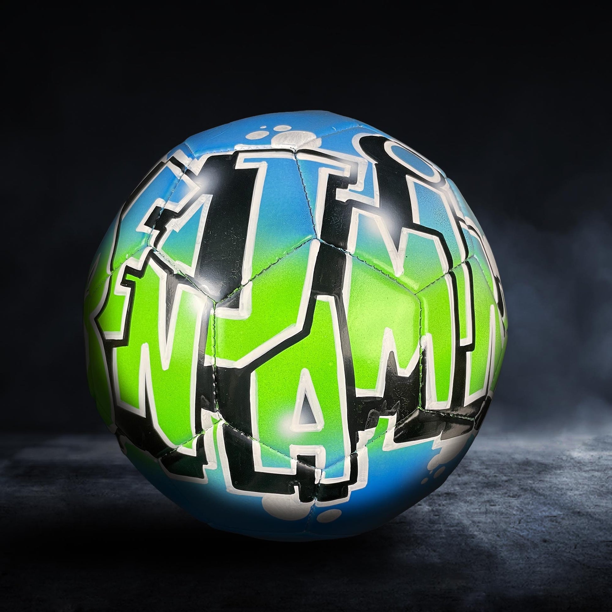 A soccer ball with the word "MAMMA" painted on it in a colorful, graffiti-style design.