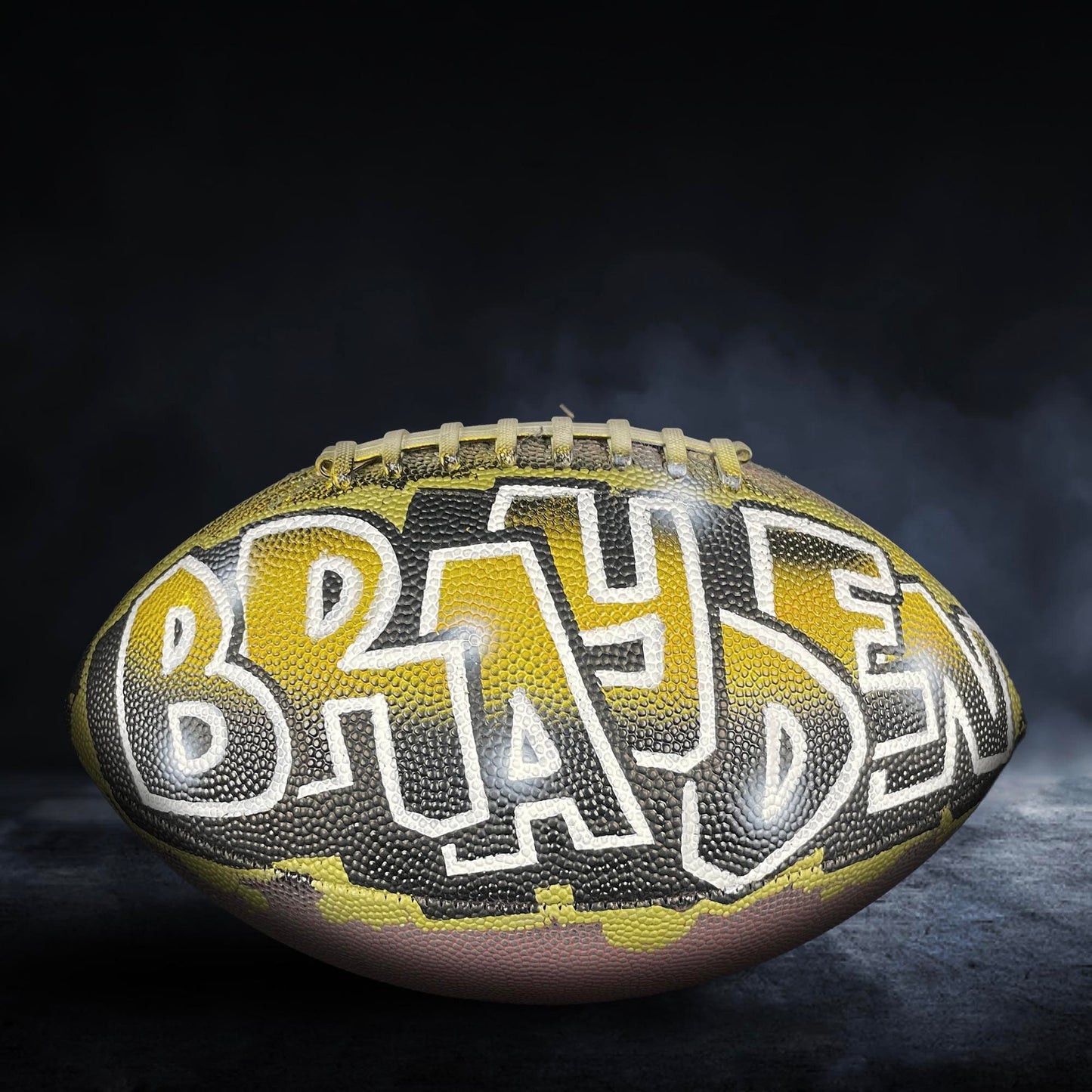 A football with the name "BRAHAM" painted on it, set against a dark background with smoke or fog.