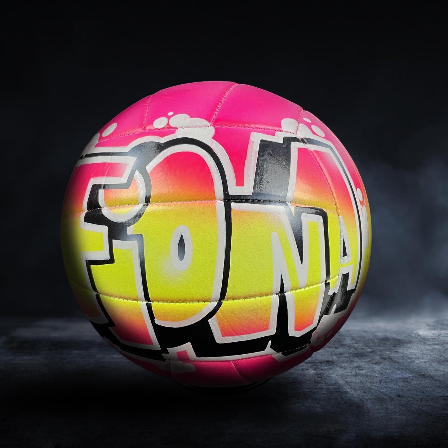 A colorful volleyball with graffiti-style text on it, set against a dark background.