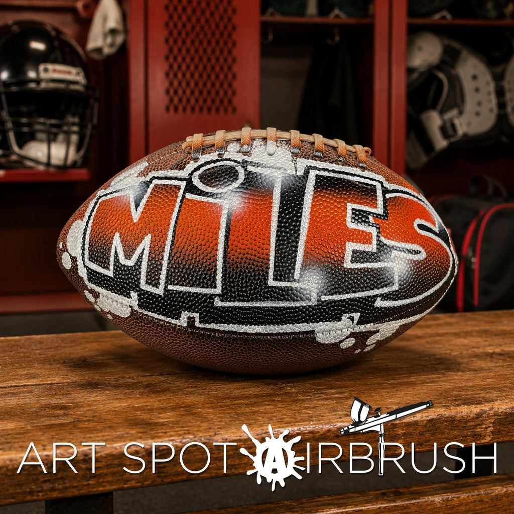 A custom football personalized with the word "MILES" painted on it, sitting on a wooden surface in a locker room.