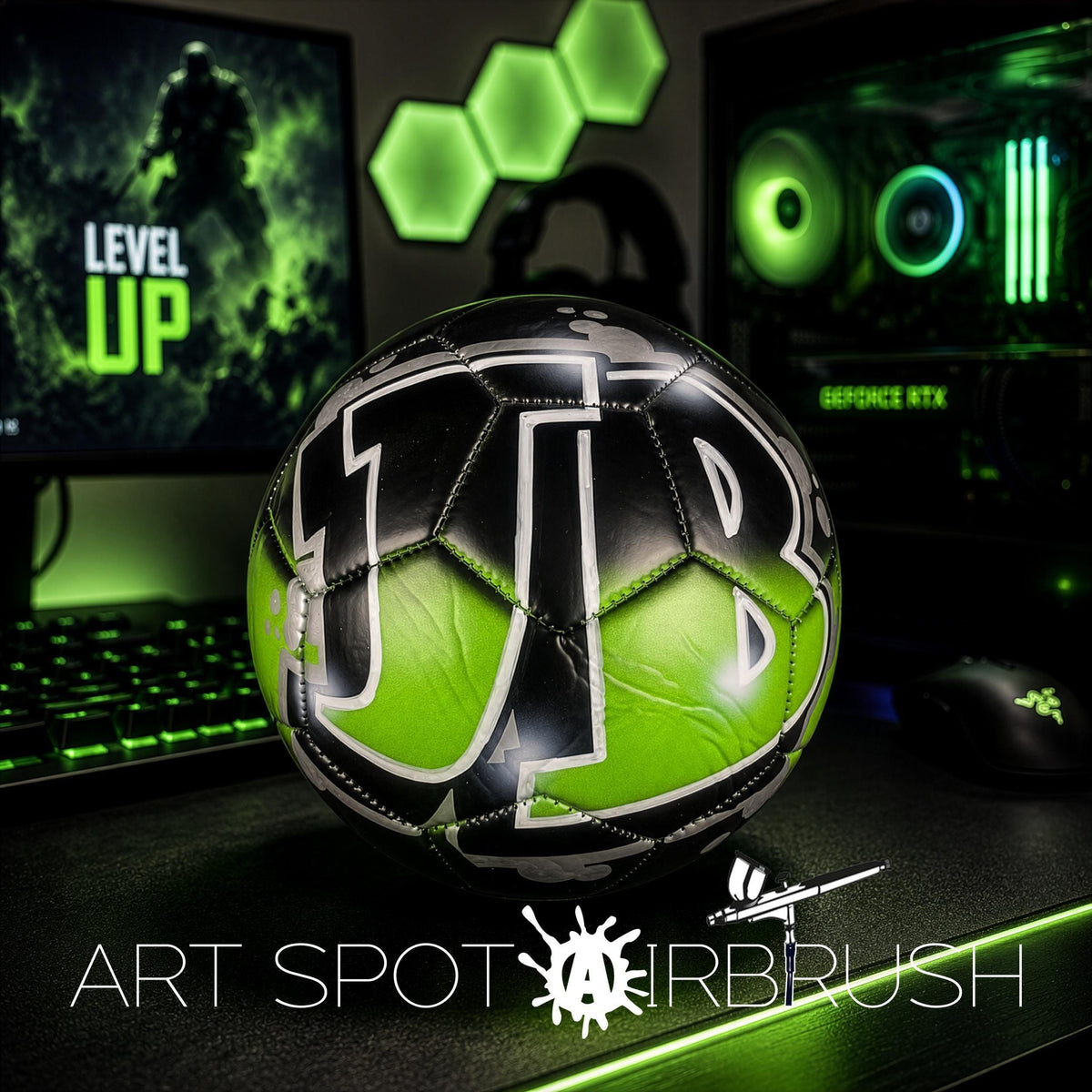 a soccer ball with the letters "JTB" on it, placed on a desk with a computer monitor, keyboard, and mouse in the background.