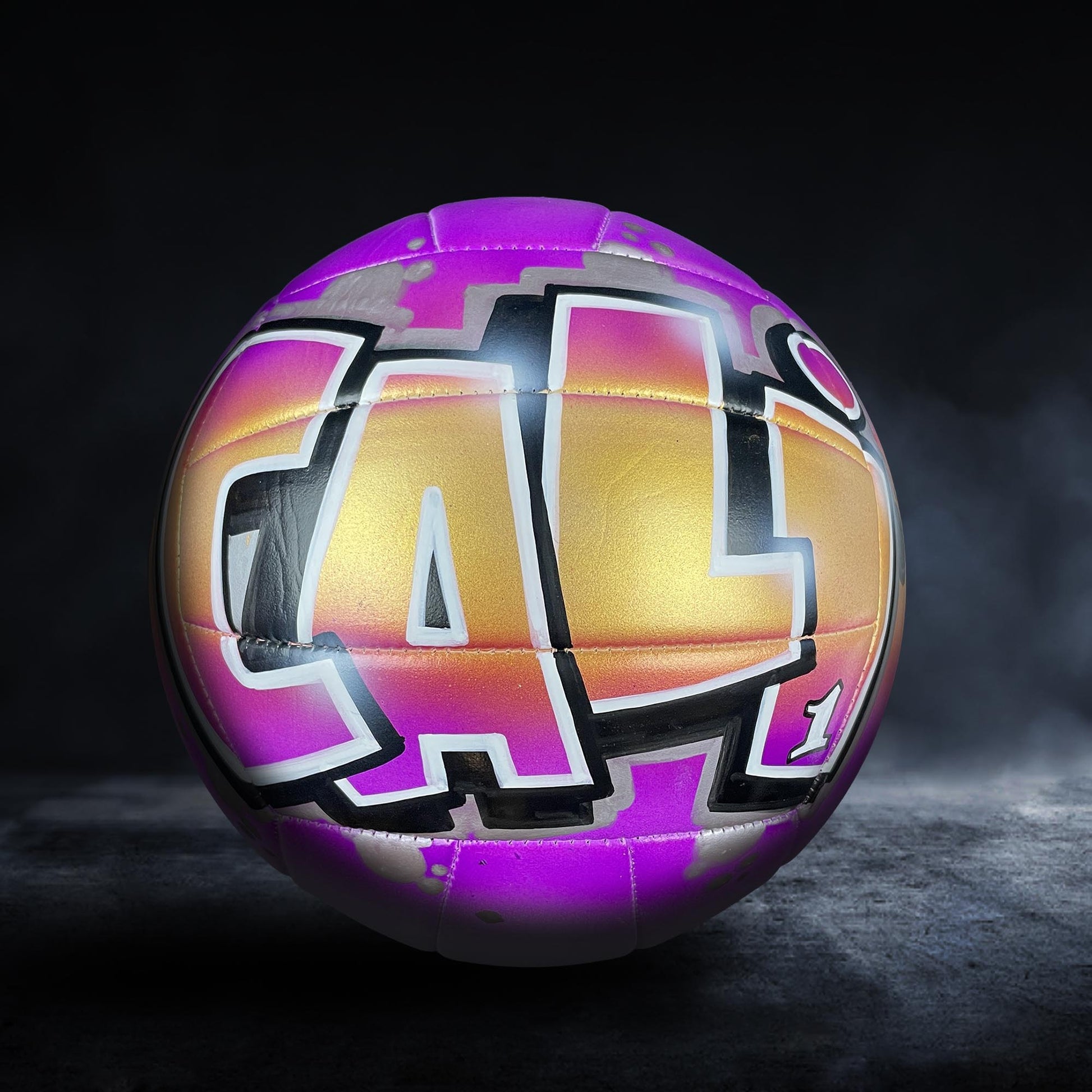 A purple and gold volleyball with the word "CAL" painted on it, set against a dark background with a misty effect.