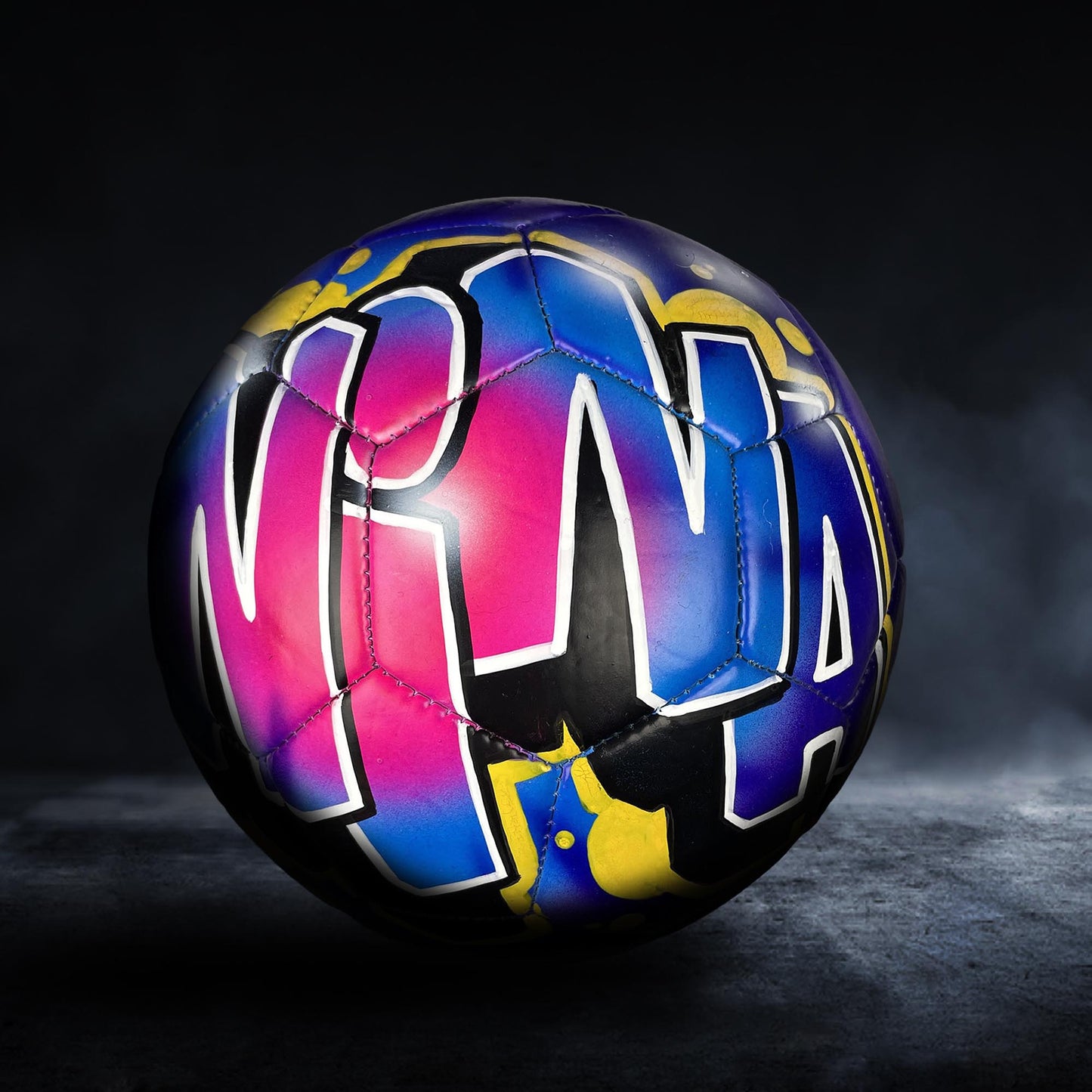 A colorful soccer ball with the word "NIA" painted on it, set against a dark background.
