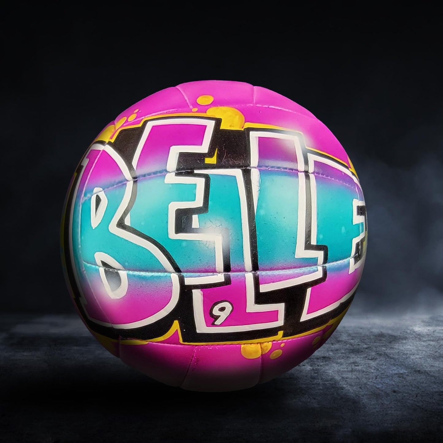 A colorful volleyball with the word "BELL" painted on it, set against a dark background.