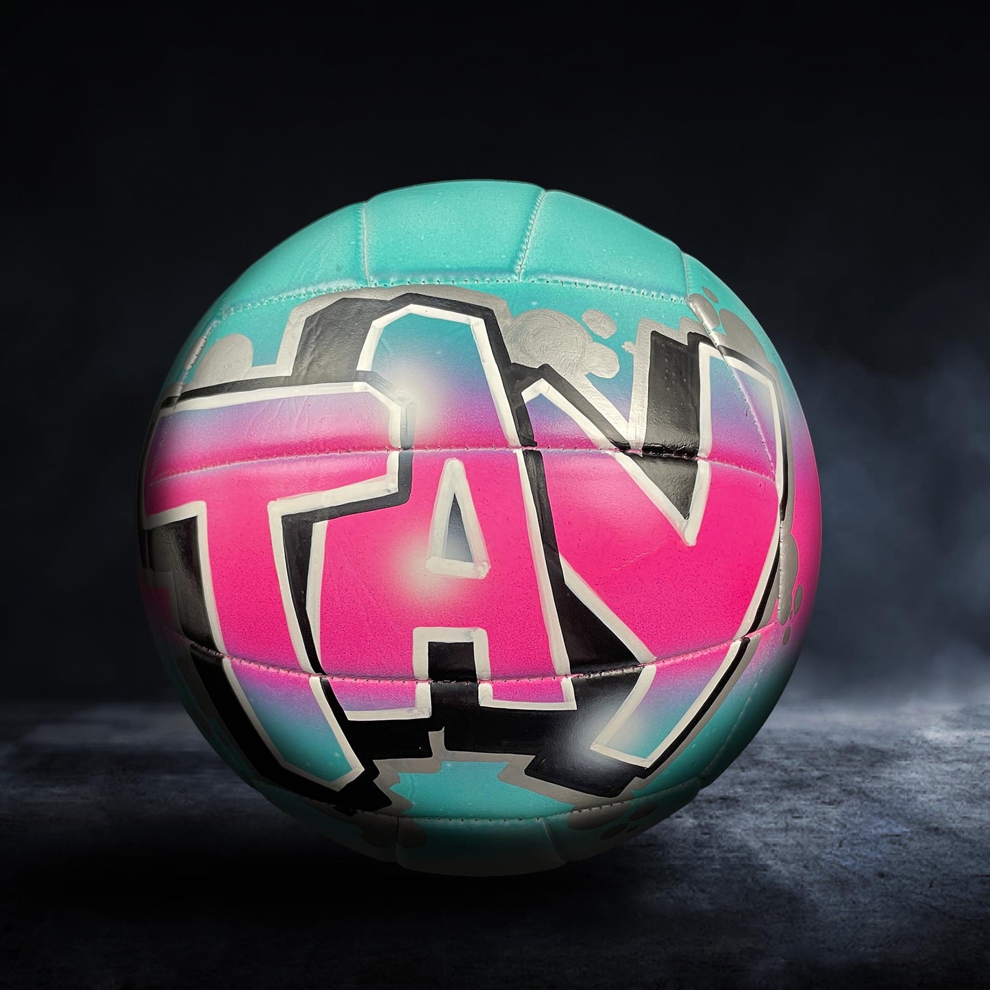 A colorful volleyball with the word "TAX" painted on it, set against a dark background.