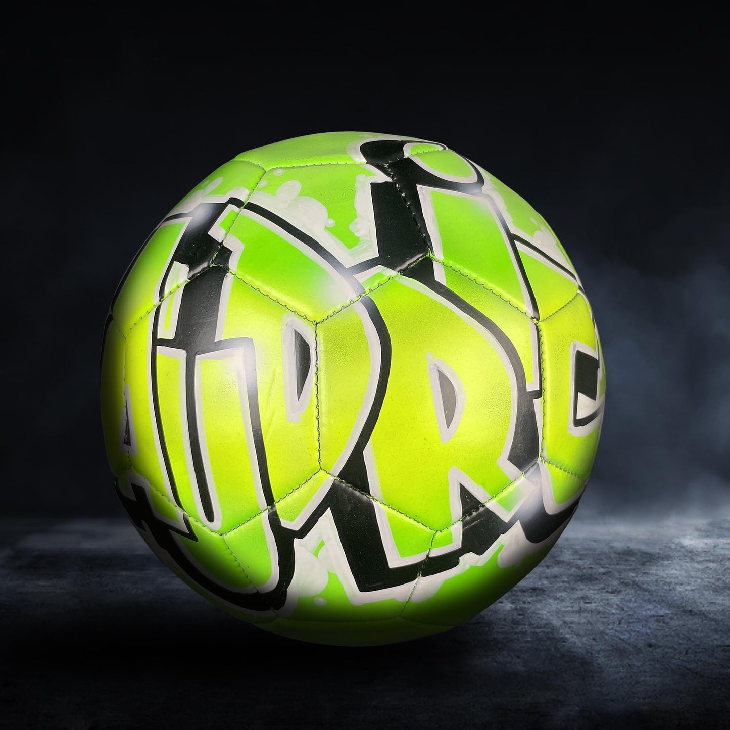 A neon green and black soccer ball with graffiti-style text on it, set against a dark background.