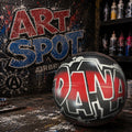 A basketball with the word "DANA" painted on it, sitting on a cluttered surface with a graffiti-covered wall in the background.