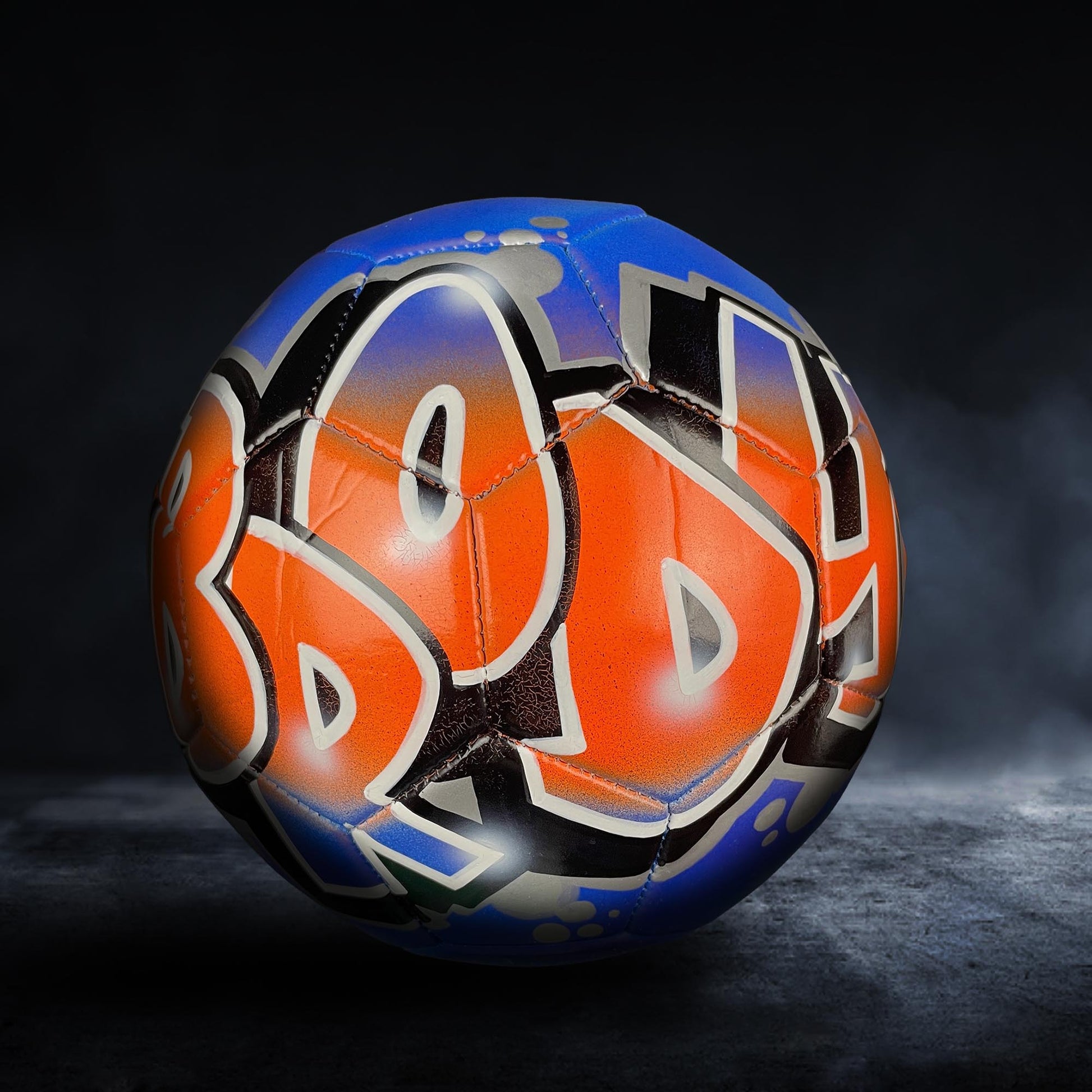 A colorful soccer ball with graffiti-style lettering on it, set against a dark background.