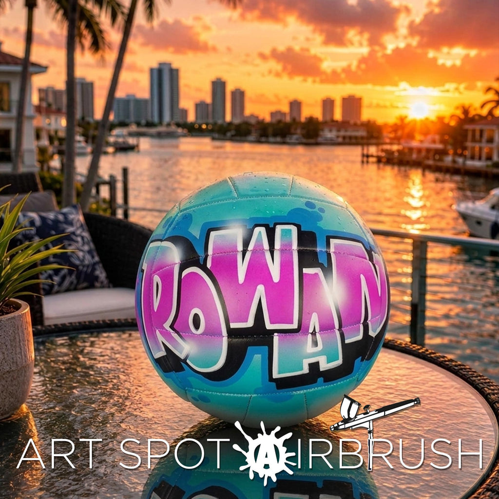 A colorful, graffiti-style volleyball with the word "Rowan" painted on it, set against a backdrop of a city skyline at sunset.