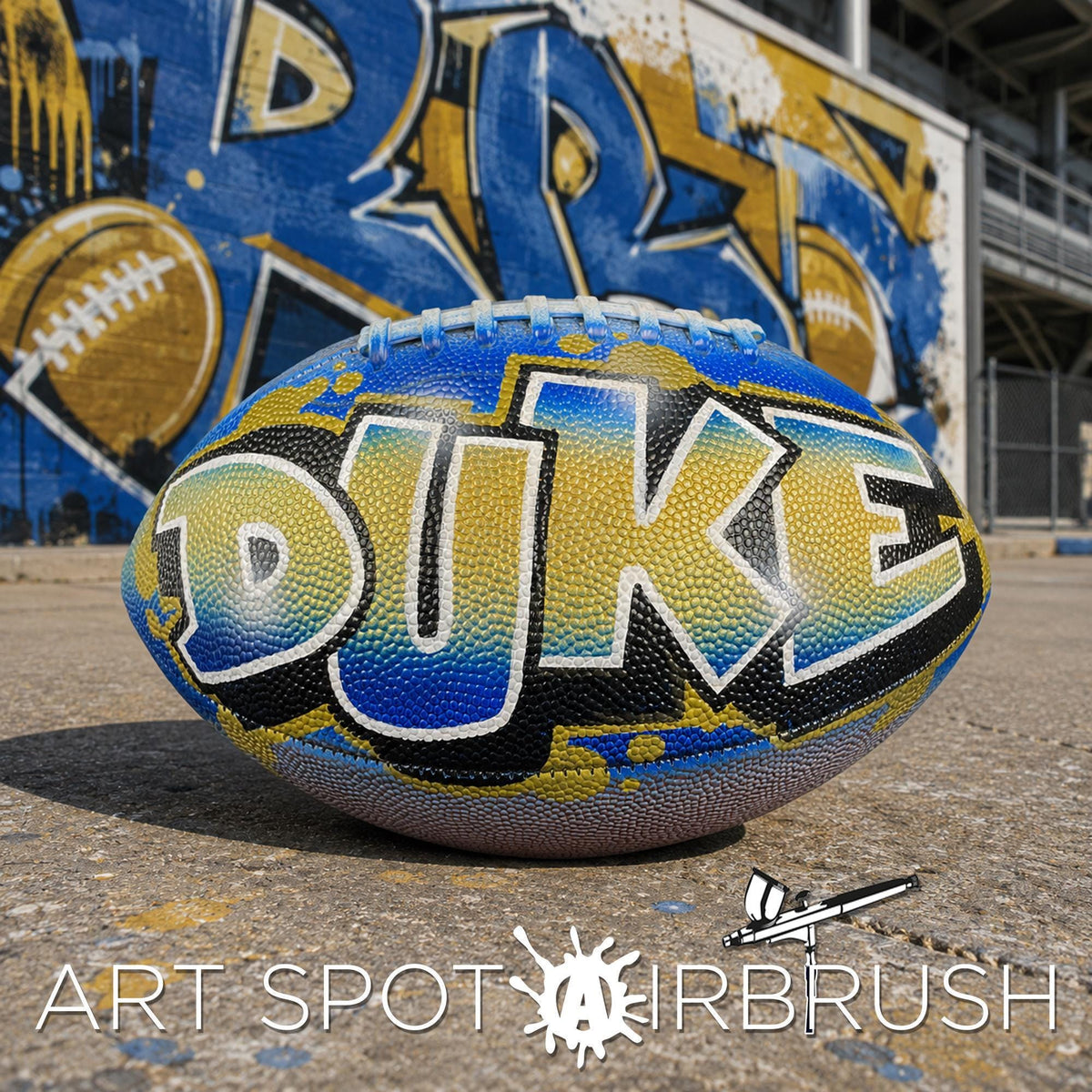 A personalized custom football with the word "DUKE" painted on it, sitting on a concrete surface in front of a graffiti-covered wall.