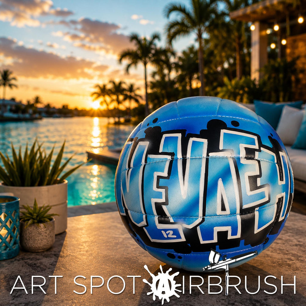 A blue and black personalized custom volleyball with the word "NEVAEH" on it, placed on a table near a pool and palm trees, with a sunset in the background.