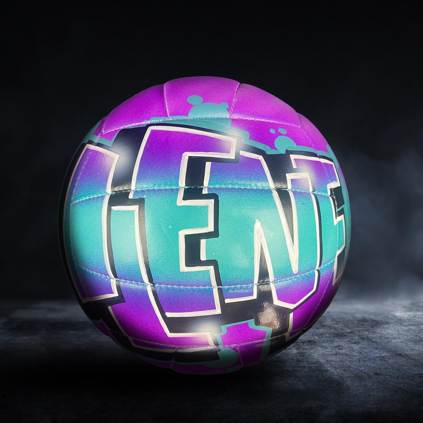 A colorful, graffiti-style soccer ball with the word "LEN" painted on it, set against a dark background.