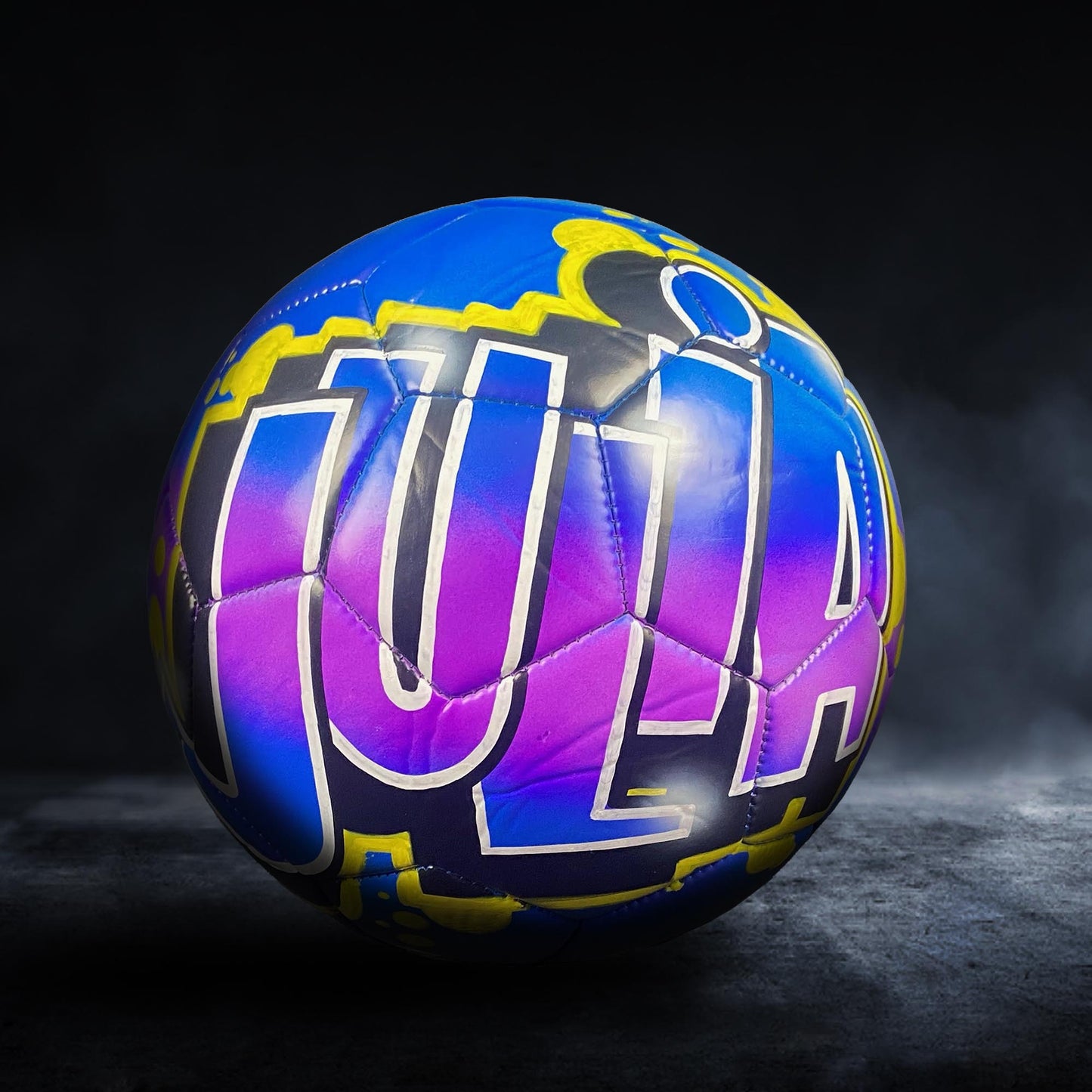 A colorful soccer ball with the name "JULIA" painted on it.