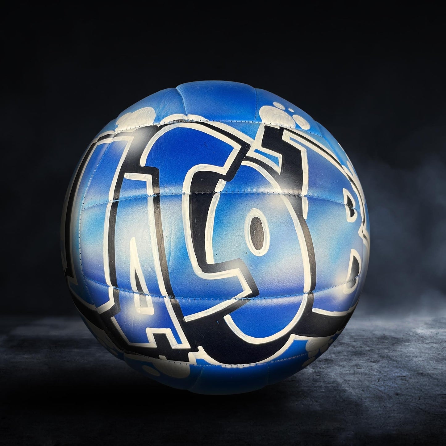 A blue and white sports ball with the word "ICOR" painted on it, sitting on a dark surface.