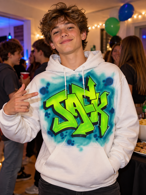 A young man wearing a white hoodie with a colorful graffiti design on it, smiling and making a peace sign gesture.