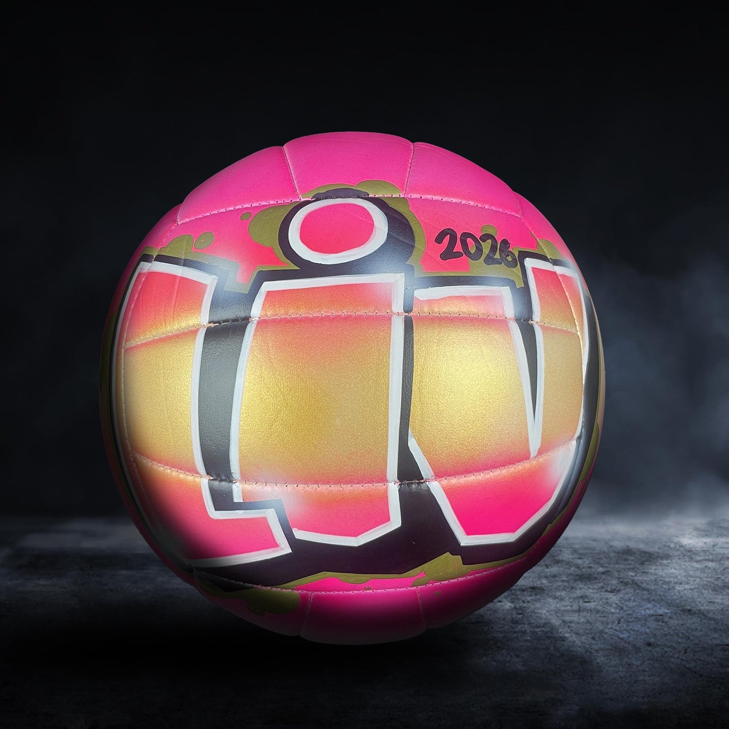 A pink and yellow volleyball with the text "LIV" on it, standing on a dark surface.