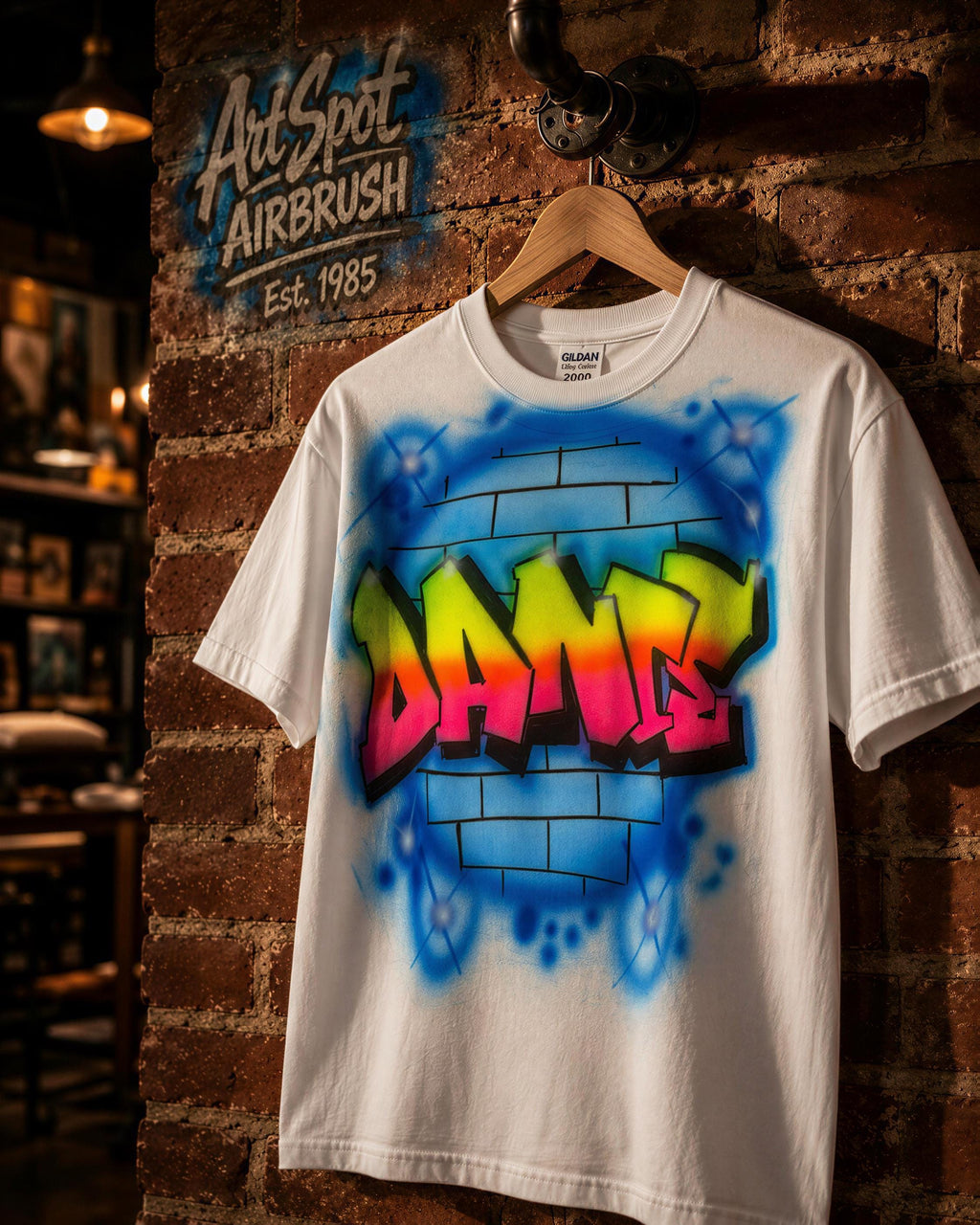 A white t-shirt with a colorful graffiti design on it, hanging on a wooden hanger against a brick wall.