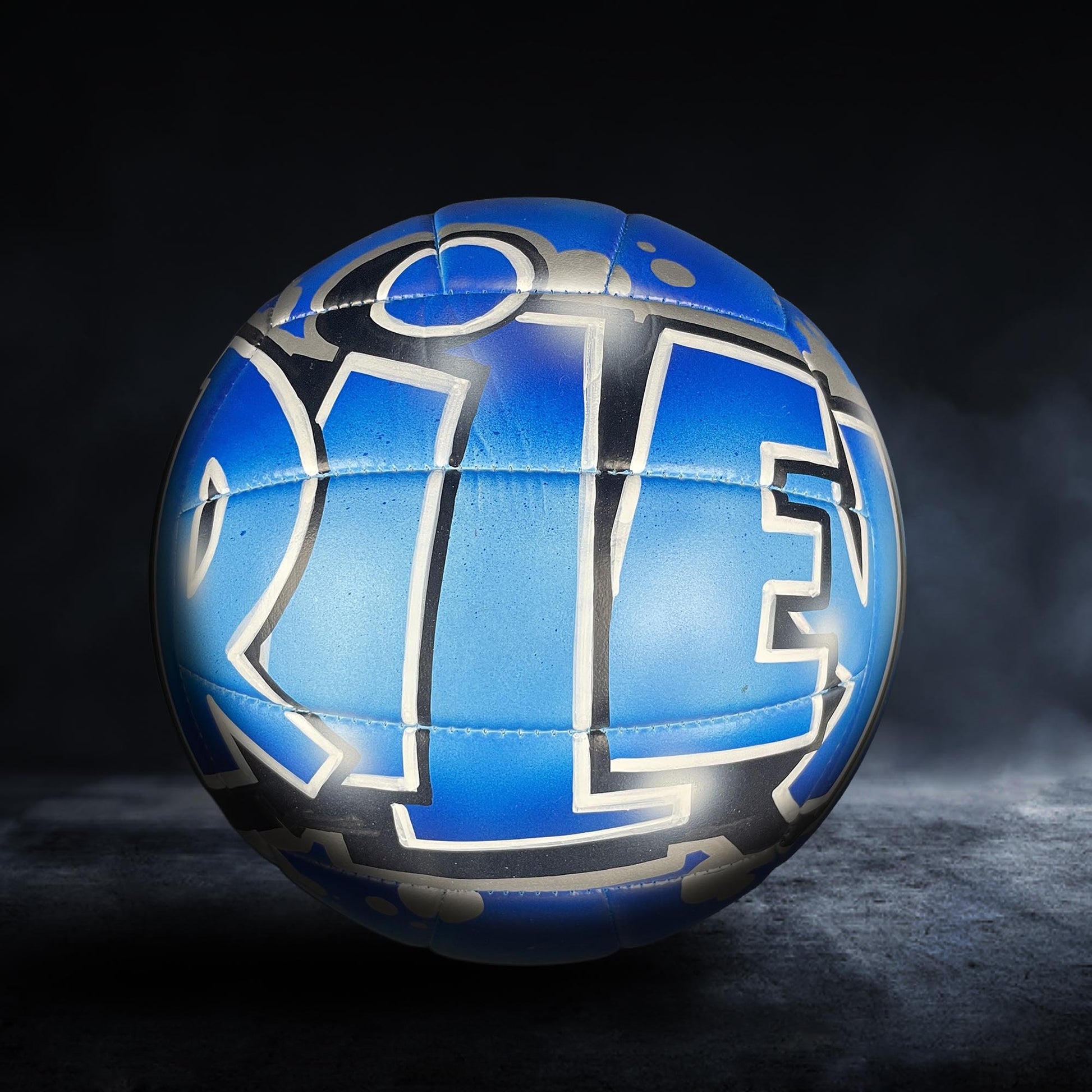 A blue and black soccer ball with graffiti-style text on it, set against a dark background.