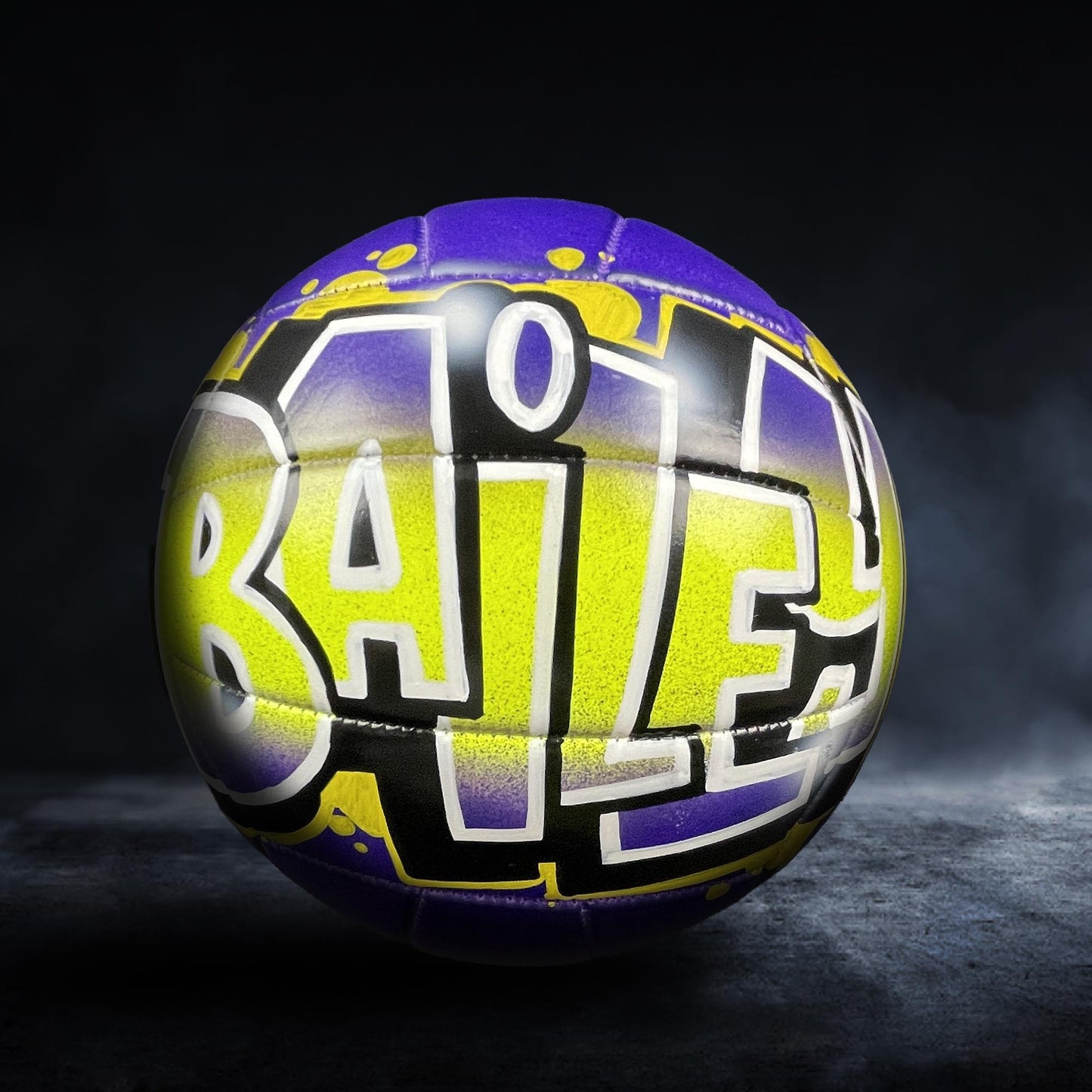 A colorful sports ball with the word "BAILEY" painted on it, set against a dark background.