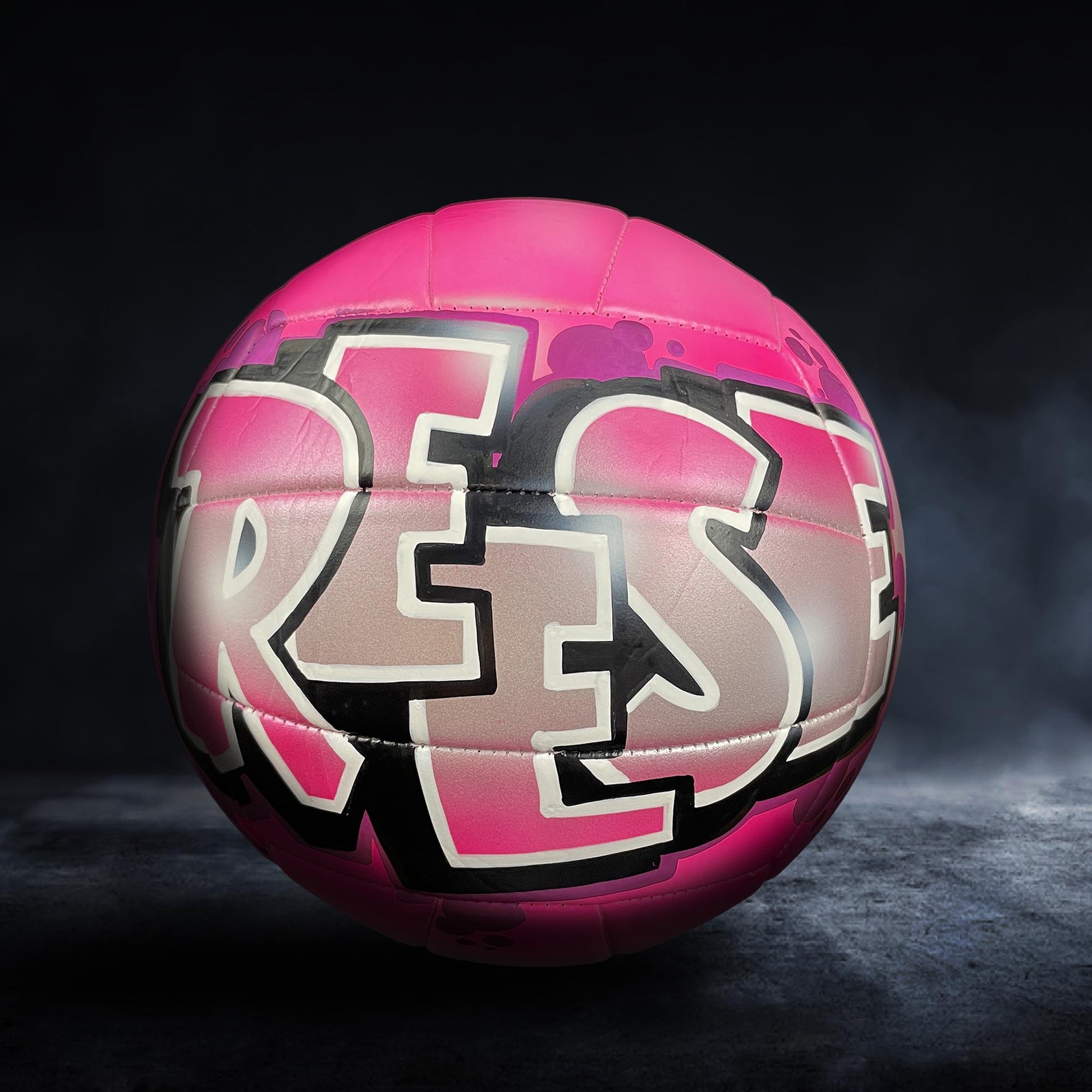 A pink volleyball with the word "RES" painted on it, against a dark background.