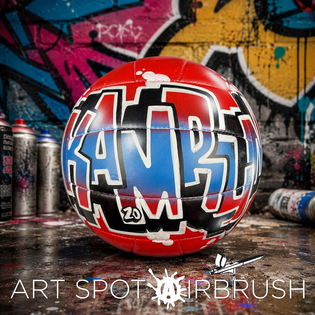 A red and blue custom volleyball personalized with graffiti text on it, placed on a surface with graffiti art in the background.