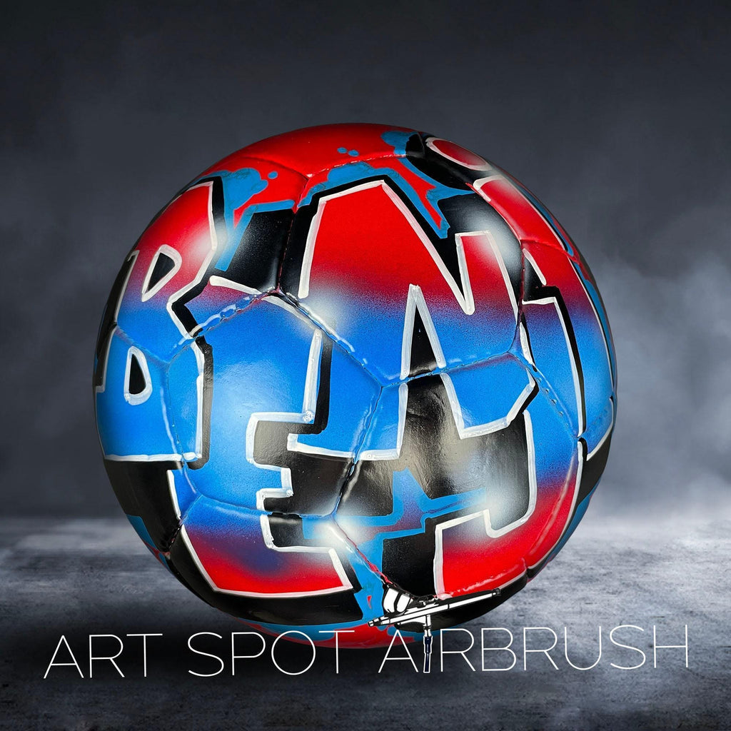 A colorful soccer ball with graffiti-style lettering on it, placed on a dark surface.