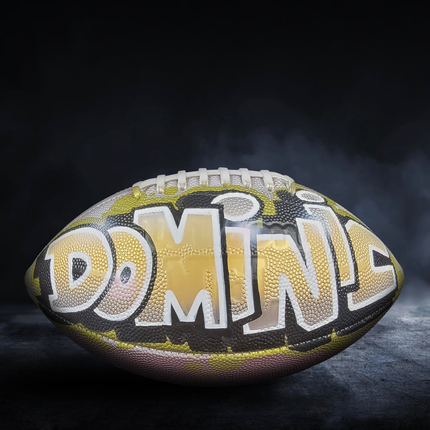 A football with the word "DOMIN" written on it, against a dark background with smoke or fog.