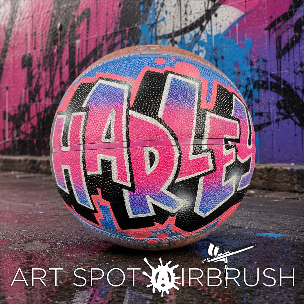 A colorful basketball with the word "HARLEY" painted on it, sitting on a surface against a graffiti-covered wall.