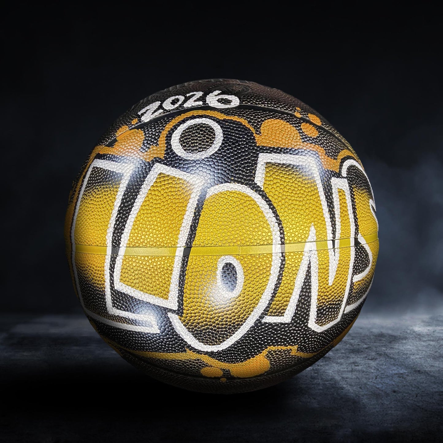 A basketball with the word "LIONS" painted on it, featuring a black and yellow color scheme.