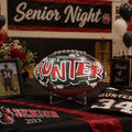 a decorated football with the name "Hunter" on it, placed on a table with a framed picture, a jersey, and balloons.