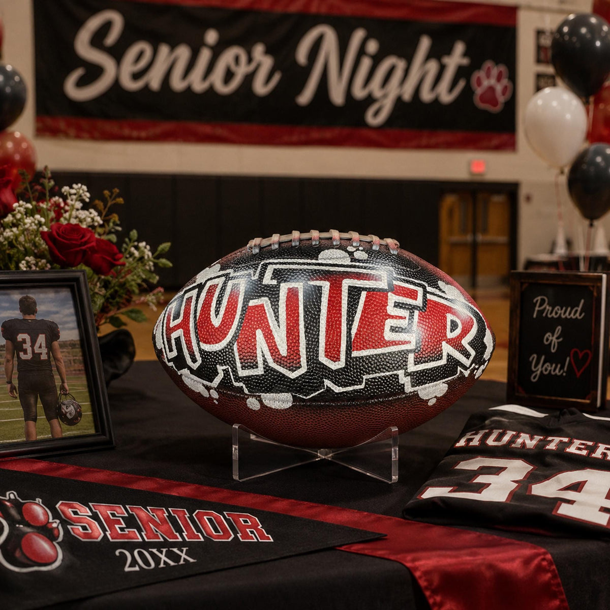 a decorated football with the name "Hunter" on it, placed on a table with a framed picture, a jersey, and balloons.
