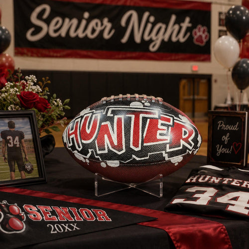a decorated football with the name "Hunter" on it, placed on a table with a framed picture, a jersey, and balloons.