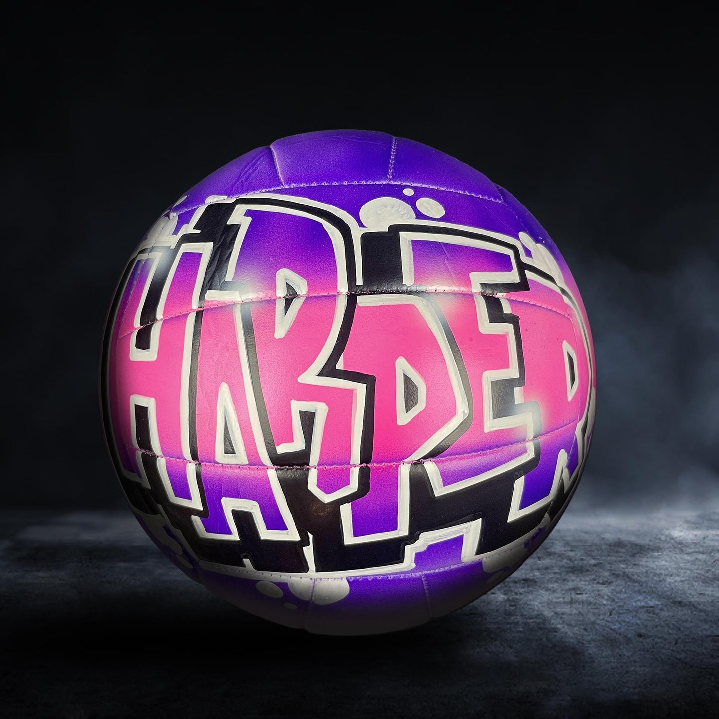 A purple and pink volleyball with the word "HARPER" written on it in graffiti-style lettering.