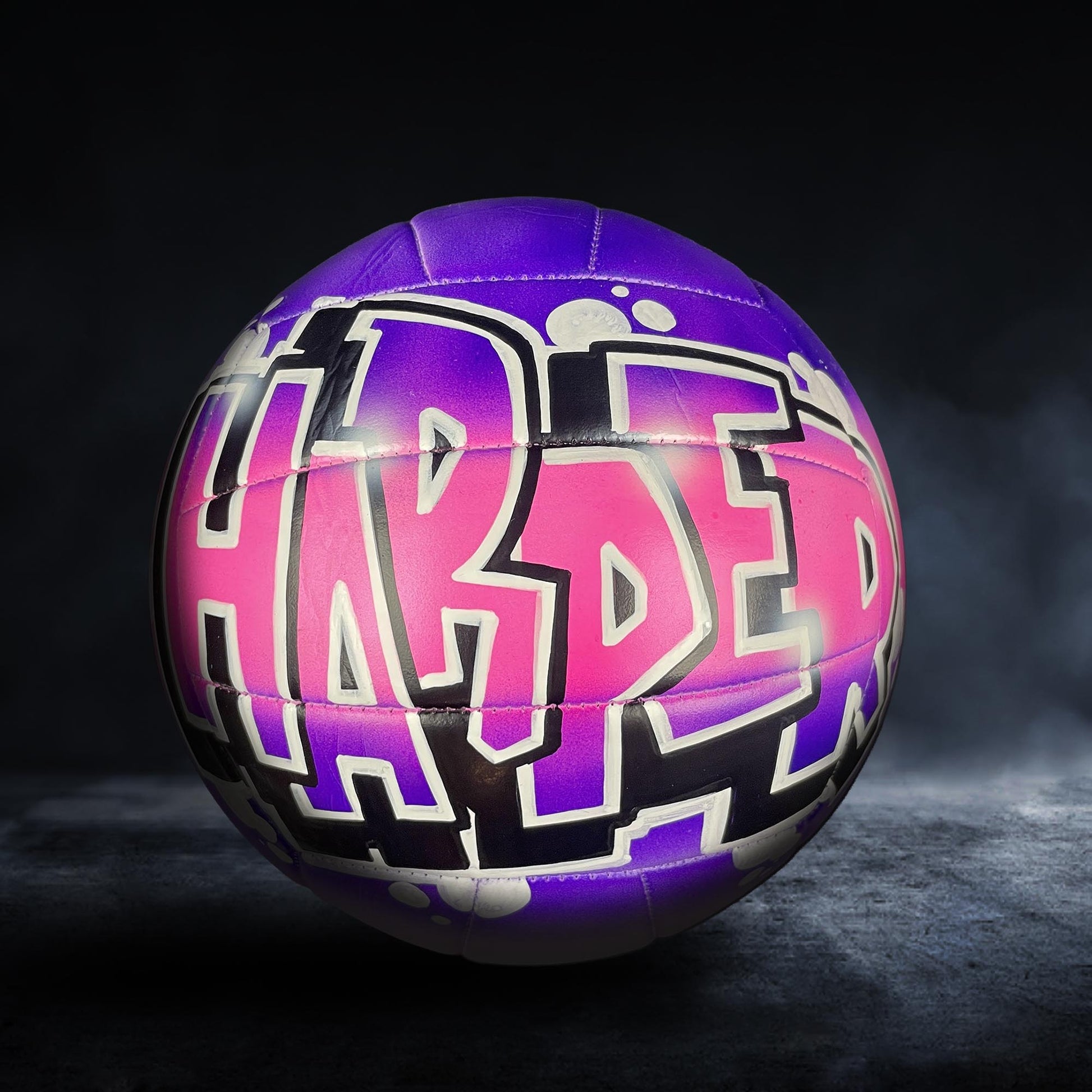 A purple and pink volleyball with the word "HARPER" written on it in graffiti-style lettering.